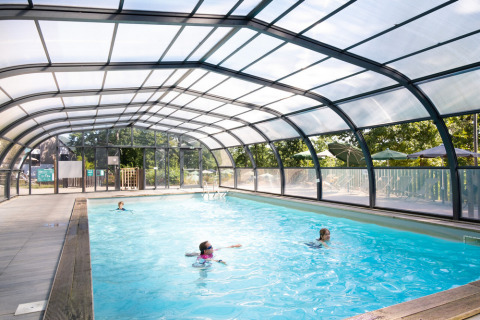 Piscina coperta con tetto trasparente e persone che nuotano a Huttopia Wattwiller, Grand Est, Francia.