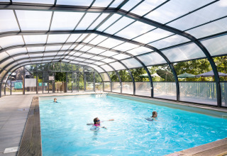 Indendørs swimmingpool med gennemsigtigt tag og mennesker, der svømmer, i Huttopia Wattwiller i Grand Est.