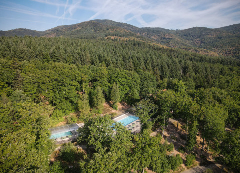 Vista aérea del parque vacacional Huttopia Wattwiller en Grand Est, Francia, rodeado de bosque y montañas.