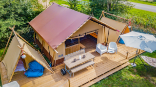 Vista aérea de la tienda safari Cozy Lodge con terraza de madera, asientos y una gran sombrilla.