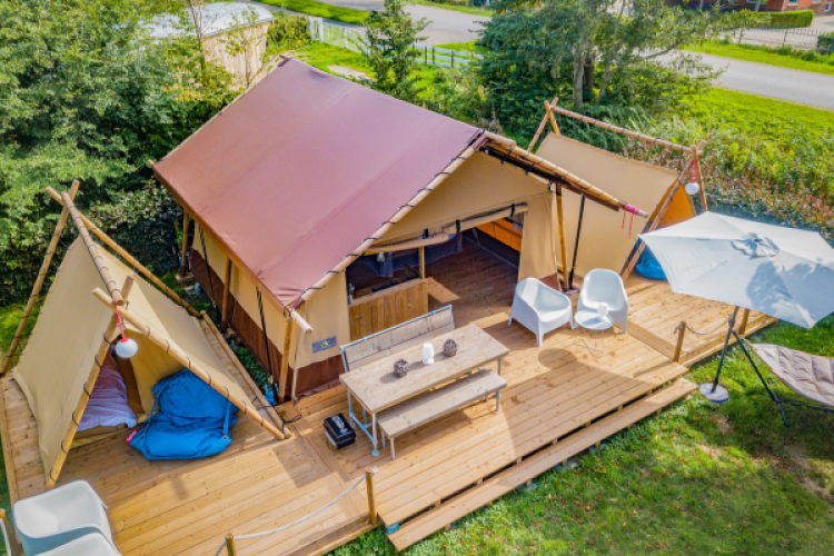Vue aérienne de la tente safari Cozy Lodge avec terrasse en bois, coins salon et grand parasol.