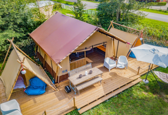 Vue aérienne de la tente safari Cozy Lodge avec terrasse en bois, coins salon et grand parasol.