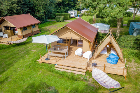 Aerial view of a Cozy Lodge safari tent with deck, seating area, hammock, and private bathroom at a campsite.