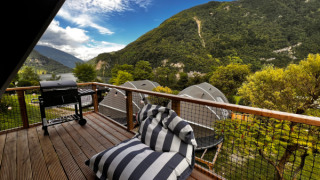 Vista dal terrazzo della tenda safari Big Oak Lodge con barbecue, poltrona a righe e monti sullo sfondo.