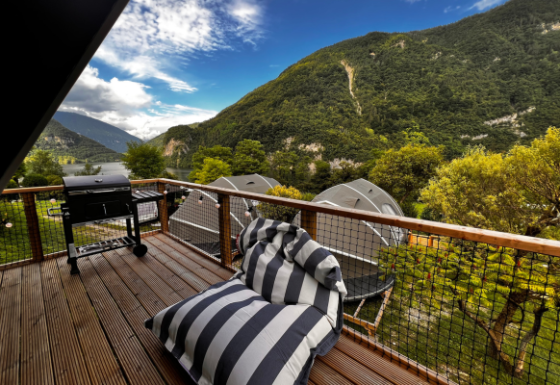 Vista dal terrazzo della tenda safari Big Oak Lodge con barbecue, poltrona a righe e monti sullo sfondo.