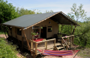 Tienda safari Wood Lodge en Camping Casa Tartufo en Italia, con terraza de madera y hamaca entre árboles.