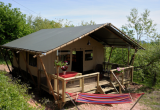 Tienda safari Wood Lodge en Camping Casa Tartufo en Italia, con terraza de madera y hamaca entre árboles.