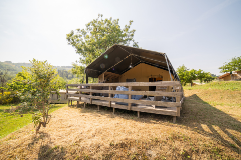 Safari Lodge Zelt mit eigenem Bad auf einer erhöhten Holzterrasse in einer grünen, hügeligen Landschaft.