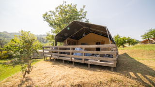 Safari Lodge tent with private bathroom set on a raised wooden deck, surrounded by lush greenery and hills.