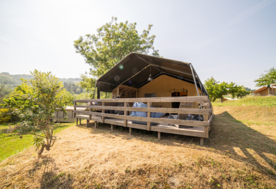 Tienda Safari Lodge con baño privado en una tarima de madera elevada, rodeada de naturaleza y colinas verdes.