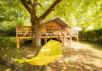 Tienda Safari Lodge + Teeny Lodge en Camping Les Tailladis, Francia, con terraza de madera y hamaca amarilla.