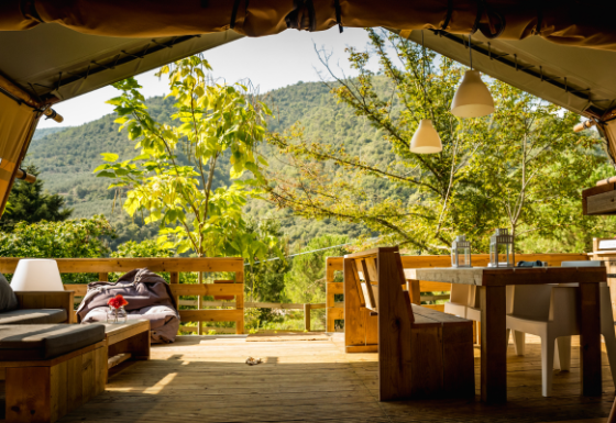 Vista desde una tienda safari Desert Lodge con mobiliario rústico de madera y paisaje montañoso verde.