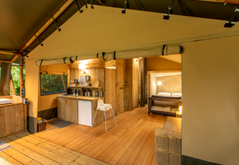 Interior de una tienda safari llamada Wood Lodge con suelos de madera, cocina y cama doble acogedora.