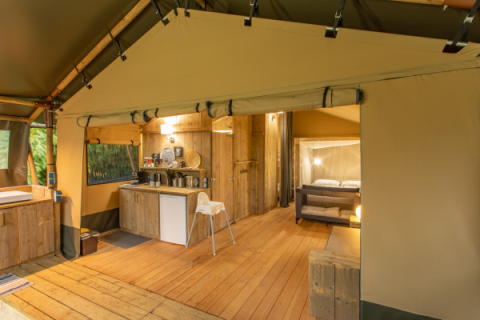 Interno di una tenda safari chiamata Wood Lodge con pavimento in legno, angolo cucina e camera da letto.