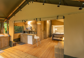 Interior of a safari tent named Wood Lodge featuring wooden floors, kitchenette, and a cozy bedroom.