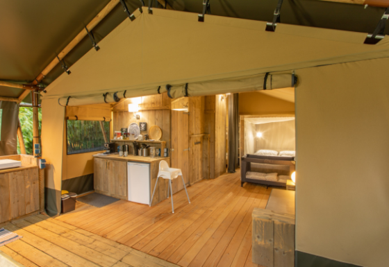 Interior de una tienda safari llamada Wood Lodge con suelos de madera, cocina y cama doble acogedora.
