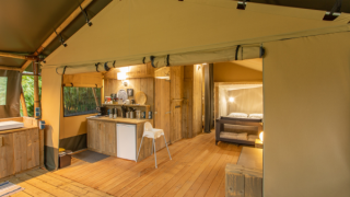 Interior de una tienda safari llamada Wood Lodge con suelos de madera, cocina y cama doble acogedora.