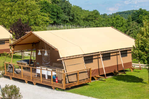 Questa foto mostra una tenda safari Desert Lodge con veranda in legno, circondata da verde e alberi.