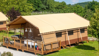 Esta foto muestra una tienda de safari Desert Lodge con terraza de madera, rodeada de vegetación y árboles.
