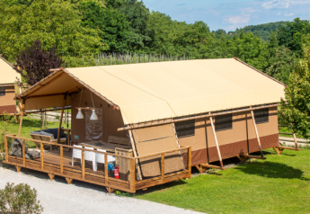 Esta foto muestra una tienda de safari Desert Lodge con terraza de madera, rodeada de vegetación y árboles.