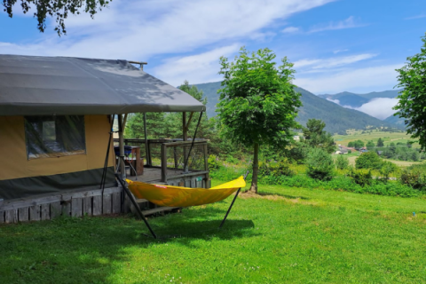 Safari tent with a deck and yellow hammock overlooking a lush green valley and scenic mountains behind.