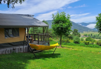 Safari tent with a deck and yellow hammock overlooking a lush green valley and scenic mountains behind.