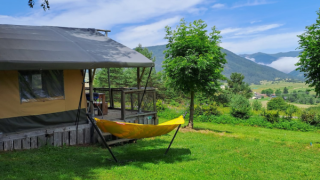 Safari tent with a deck and yellow hammock overlooking a lush green valley and scenic mountains behind.