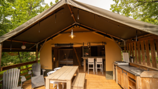 Safari Lodge safaritent met houten terras, eettafel, stoelen en open keuken omringd door groen.