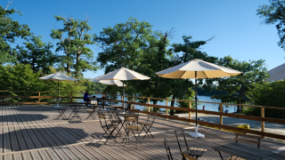Buitenterras met parasols en tafels aan een meer bij Camping Seasonova L'Etang des Bois, Centre-Val de Loire.