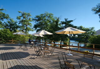 Buitenterras met parasols en tafels aan een meer bij Camping Seasonova L'Etang des Bois, Centre-Val de Loire.