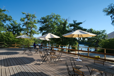 Outdoor terrace with umbrellas and tables by a lake at Camping Seasonova L'Etang des Bois, Centre-Val de Loire.