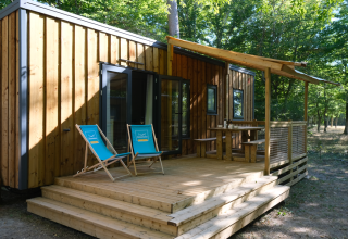 Bungalow in legno con ampia veranda e sdraio blu al Camping Seasonova L'Etang des Bois, Centre-Val de Loire, Francia.