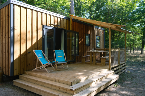 Cabaña de madera con terraza y tumbonas azules en Camping Seasonova L'Etang des Bois, Centre-Val de Loire, Francia.