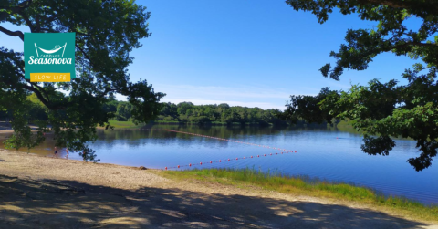 Vue sur le lac du Camping Seasonova L'Etang des Bois, avec plage de sable et arbres, en Centre-Val de Loire, France.