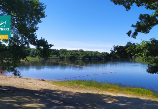 Vista sul lago al Camping Seasonova L'Etang des Bois con spiaggia sabbiosa e alberi, in Centre-Val de Loire, Francia.