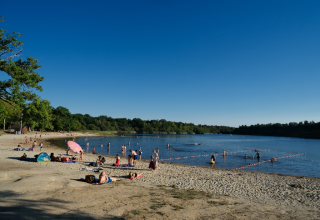 Urlauber entspannen am Sandstrand und baden im See im Camping Seasonova L'Etang des Bois, Frankreich.