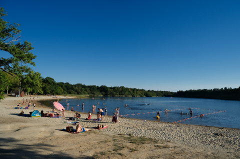 Holidaymakers relax on the sandy beach and swim in the lake at Camping Seasonova L'Etang des Bois, France.