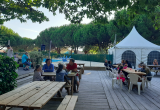 Udendørs spiseområde med træborde og familier, omgivet af træer i Village Seasonova Bassin d'Arcachon.