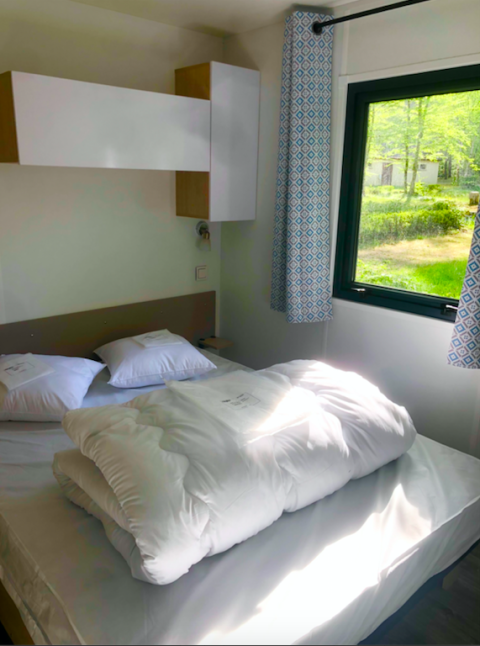 Lichte slaapkamer in een Prestique-hut op Camping Seasonova L'Etang des Bois, Frankrijk met raamzicht.