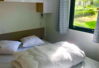 Lichte slaapkamer in een Prestique-hut op Camping Seasonova L'Etang des Bois, Frankrijk met raamzicht.