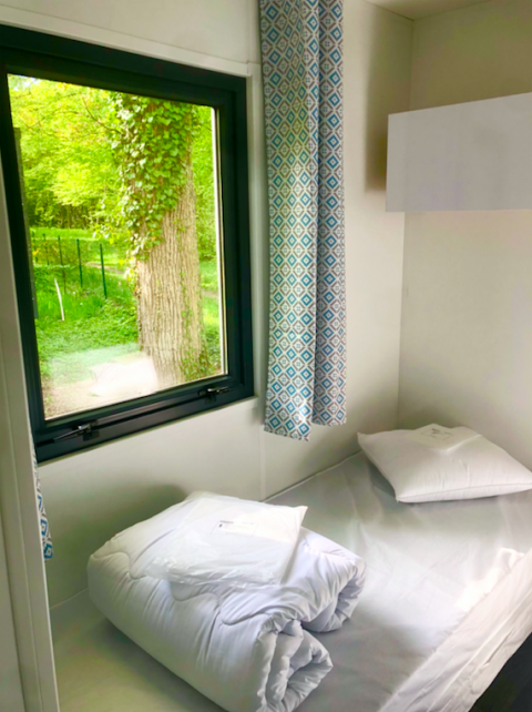 Eenvoudige kamer met bed en venster in een Prestique-hut op Camping Seasonova L'Etang des Bois, Frankrijk.