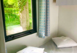 Dormitorio sencillo con cama y ventana en una cabaña Prestique en Camping Seasonova L'Etang des Bois, Francia.