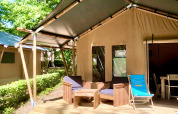 Tienda tipo safari con terraza de madera, sillones al aire libre y entorno verde bajo la luz del sol.