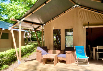 Tienda tipo safari con terraza de madera, sillones al aire libre y entorno verde bajo la luz del sol.