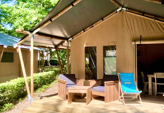 Safari-telt med træterrasse, komfortable udendørsmøbler og frodige grønne omgivelser i solen.