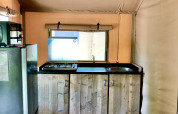 Küchenbereich in einem Safarizelt mit Holzschränken, Gasherd, Spüle und Kühlschrank auf Holzboden.