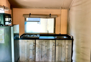 Zona cucina all'interno di una tenda safari con armadietti in legno, fornello a gas, lavello e frigorifero.