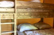 Etagenbett aus Holz mit Kissen und Decken in einem Safari-Zelt mit gelblich-braunen Wänden.