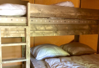Letto a castello in legno con cuscini e piumoni all'interno di una tenda safari dalle pareti calde.