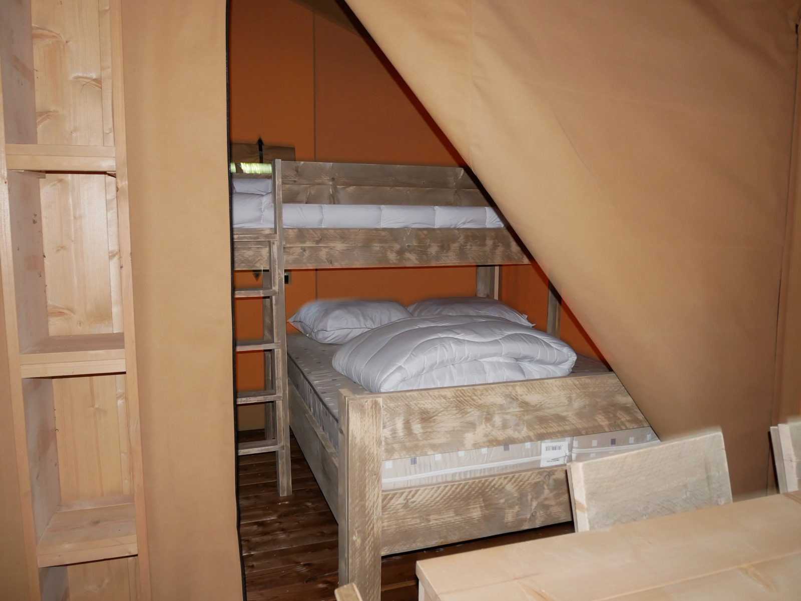 Binnenkant van een safaritent met houten stapelbed, planken en rustieke houten meubels.